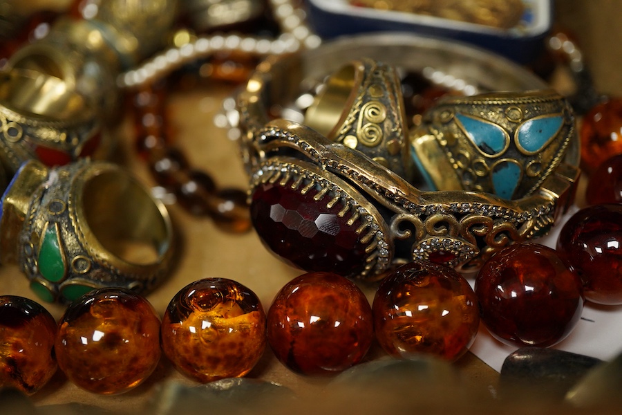A collection of costume jewels, comprising: an Egyptian-style oval medallion pendant bordered in enamel; two imitation amber necklaces; a simulant pearl necklace; a pair of floral drop earrings; five lapis rings; a bangl